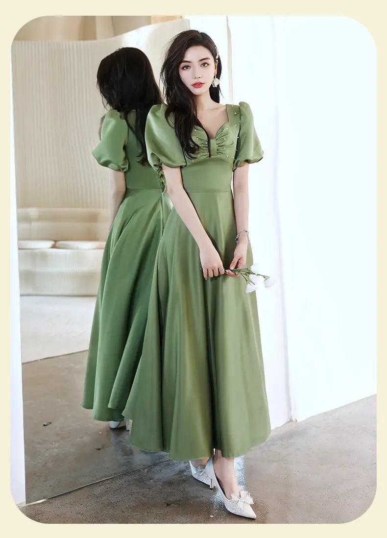 A woman wears an avocado green sisters group satin v neck midi dress featuring puffed short sleeves and a delicate embellished neckline.