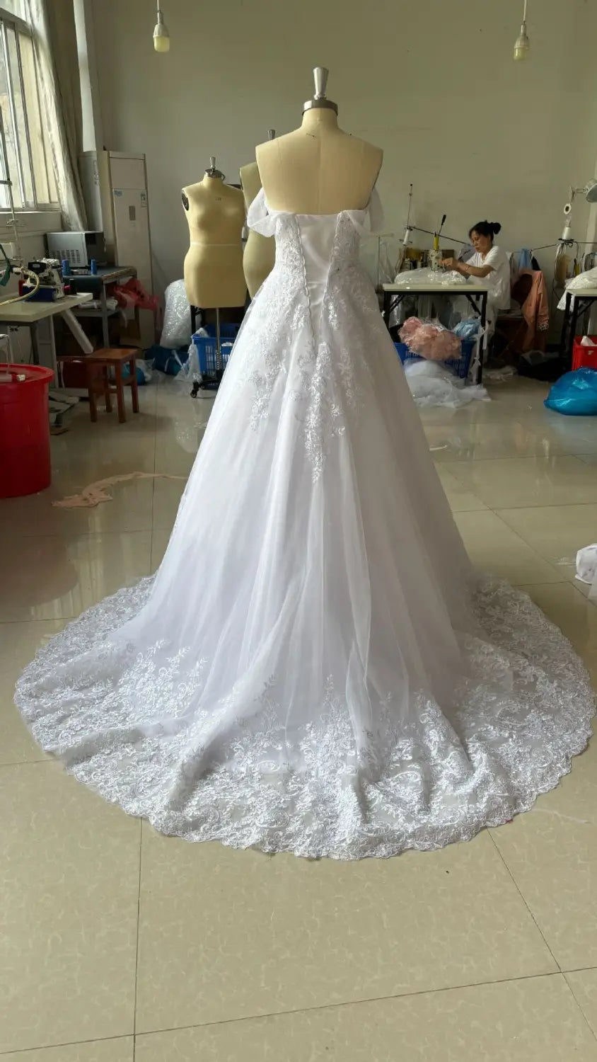 A white off-shoulder lace bridal main wedding dress with intricate lace detailing and a flowing tulle skirt displayed on a mannequin.