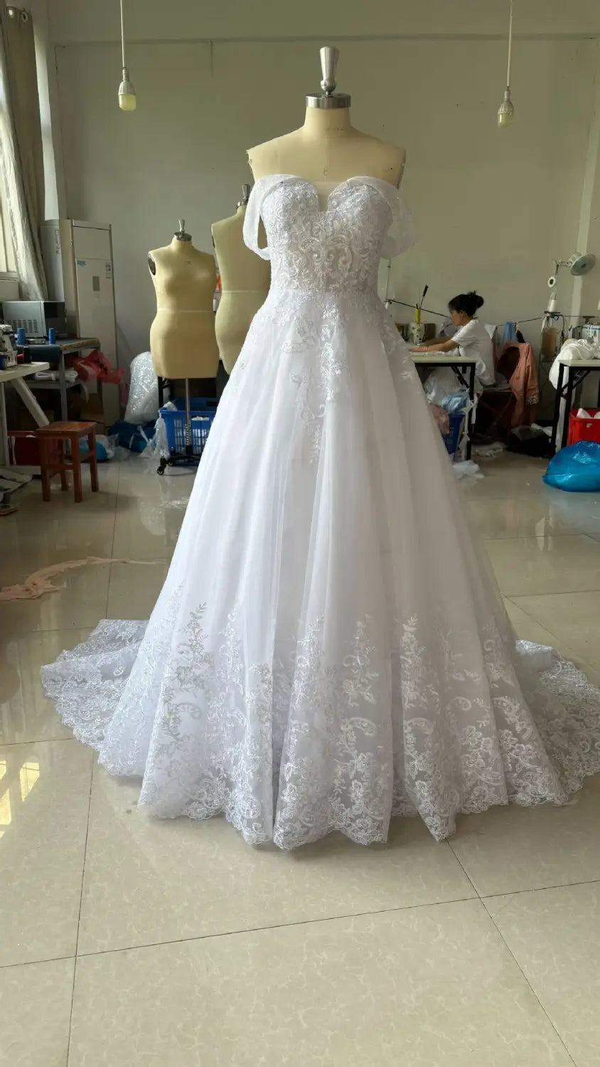 A white off-shoulder lace bridal main wedding dress featuring a sweetheart neckline and intricate floral embroidery along the bodice and skirt hem.