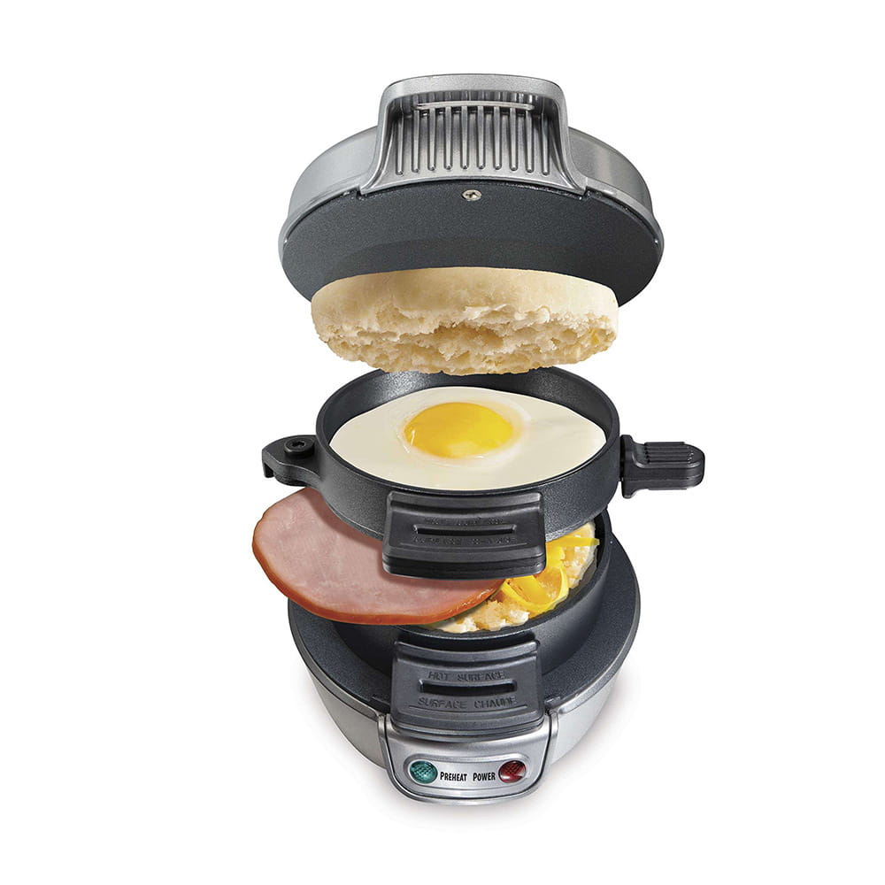 silver and black hamilton beach electric hamburger maker and egg toaster with a cooked sunny-side-up egg ham slice and scrambled eggs between two halves of a toasted english muffin featuring royale essence lux design