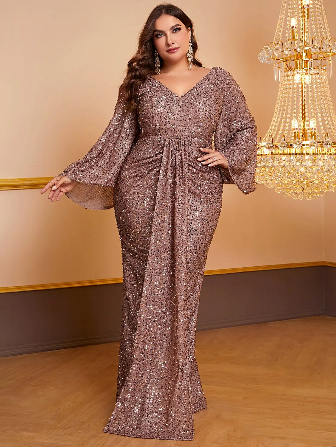 A shimmering rose gold sequin long sleeved gown featuring a v-neckline and flared sleeves designed for elegant occasions.