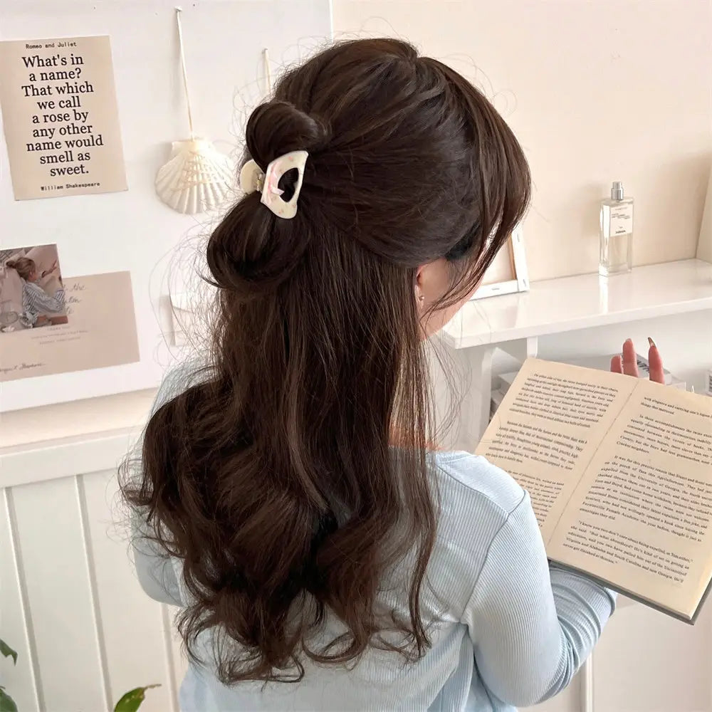 a cream-colored small jaw clip with black inner detail shaped like cat ears holding dark brown wavy hair in an elegant updo featuring a pink butterfly floral bow