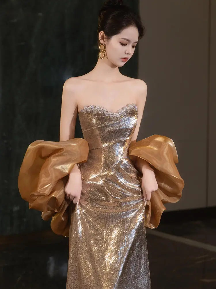 A gold sequined banquet temperament evening dress featuring a strapless gown design with voluminous satin puff sleeves.