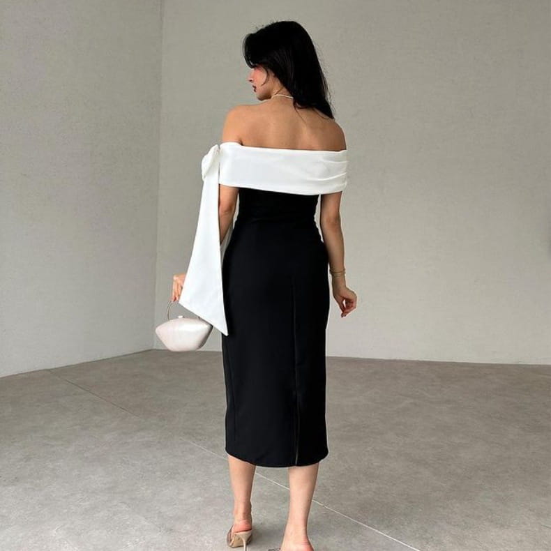black off-the-shoulder midi dress featuring a white fabric sash draped over one shoulder showcasing a white color matching elegant cocktail design