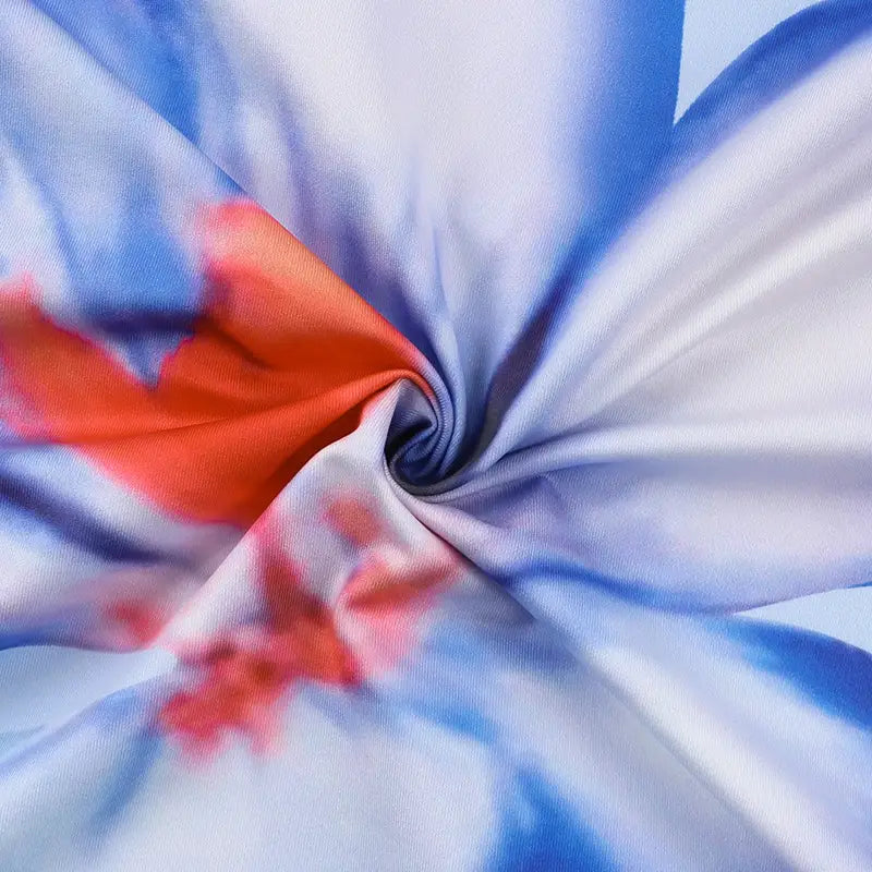 a flowing silk scarf with a vibrant blue and white gradient pattern accented by bold orange splashes complements the pink floral american style flower strap dress.