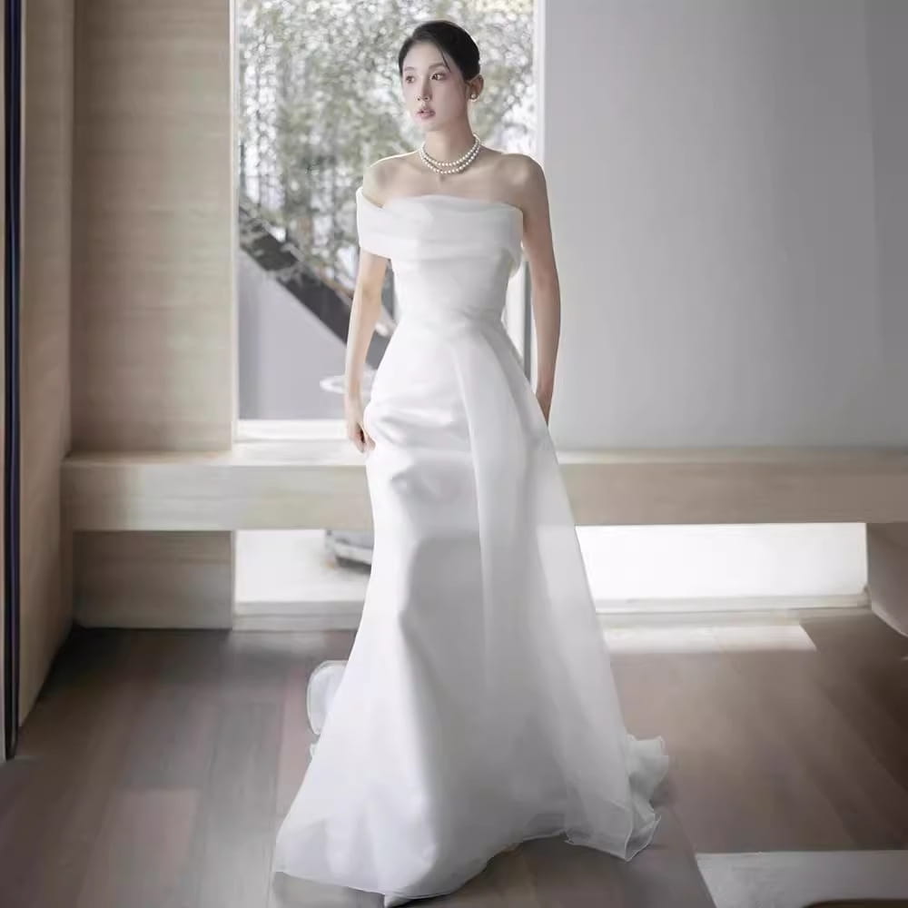 A flowing white off-shoulder satin light wedding dress with a fitted mermaid bodice and sheer overlay designed for a wedding dress bride.