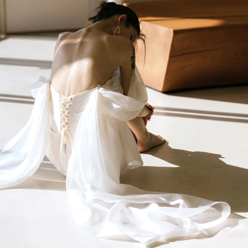 off the shoulder mini light wedding dress featuring a flowing white sheer wedding gown with a delicate lace-up back and soft billowing sleeves designed as a small light wedding dress.