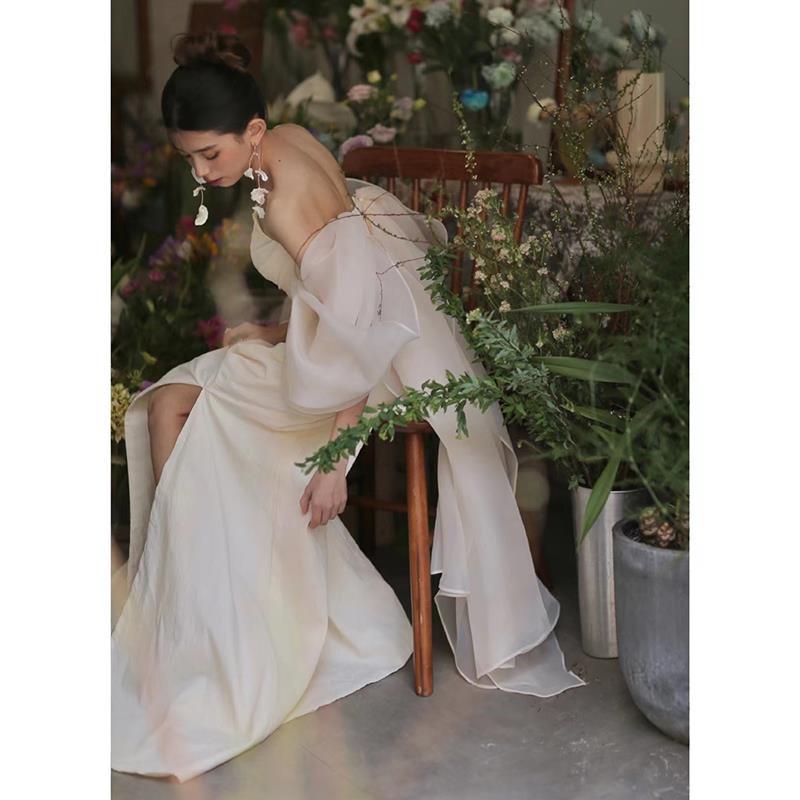 off-the-shoulder ivory satin gown with flowing sheer shooting light yarn sleeves and a high slit designed for outdoor travel shooting.