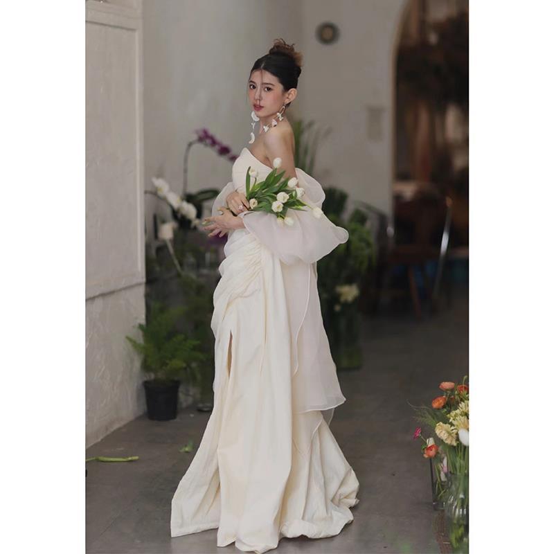 a flowing off-the-shoulder ivory satin gown with layered sheer ruffled sleeves and a high slit designed for outdoor travel shooting with light yarn fabric.