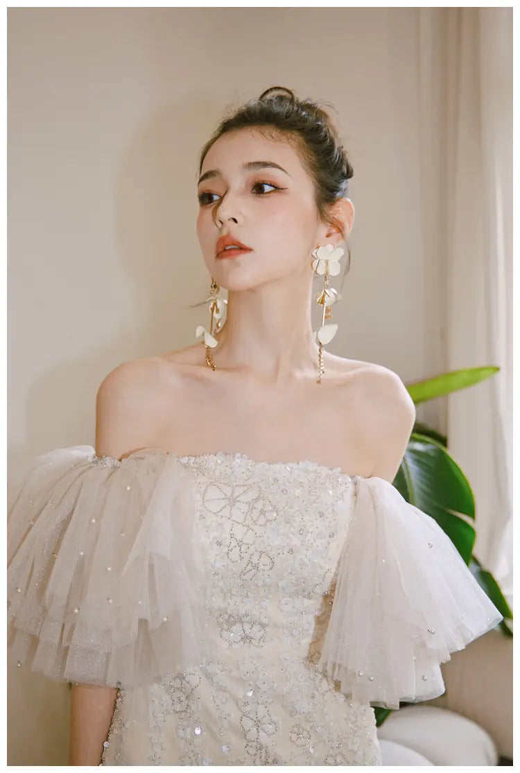 A delicate off-the-shoulder ivory lace cinched waist miniskirt fairy dress featuring intricate beading and layered tulle sleeves.