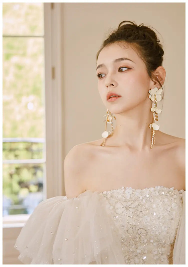 A woman wears an ivory lace cinched waist miniskirt fairy dress featuring a white off-the-shoulder gown with intricate beading and sheer tulle sleeves.