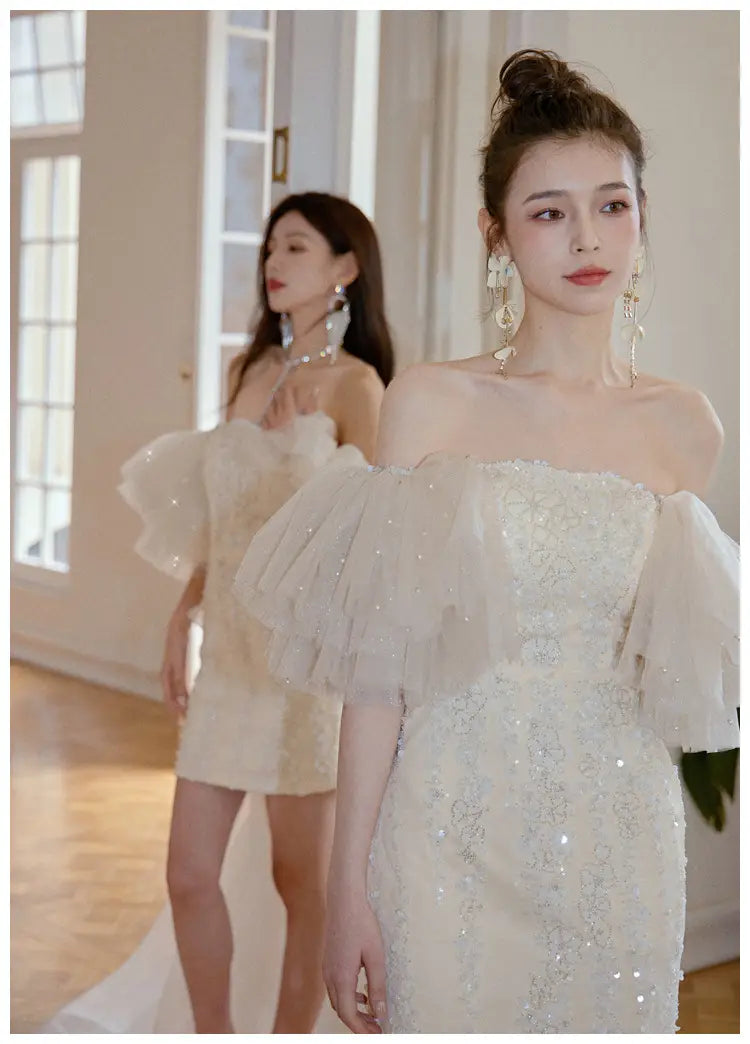 Ivory lace cinched waist miniskirt fairy dress featuring a shimmering off-the-shoulder design with intricate beaded embroidery and voluminous sheer ruffled sleeves.