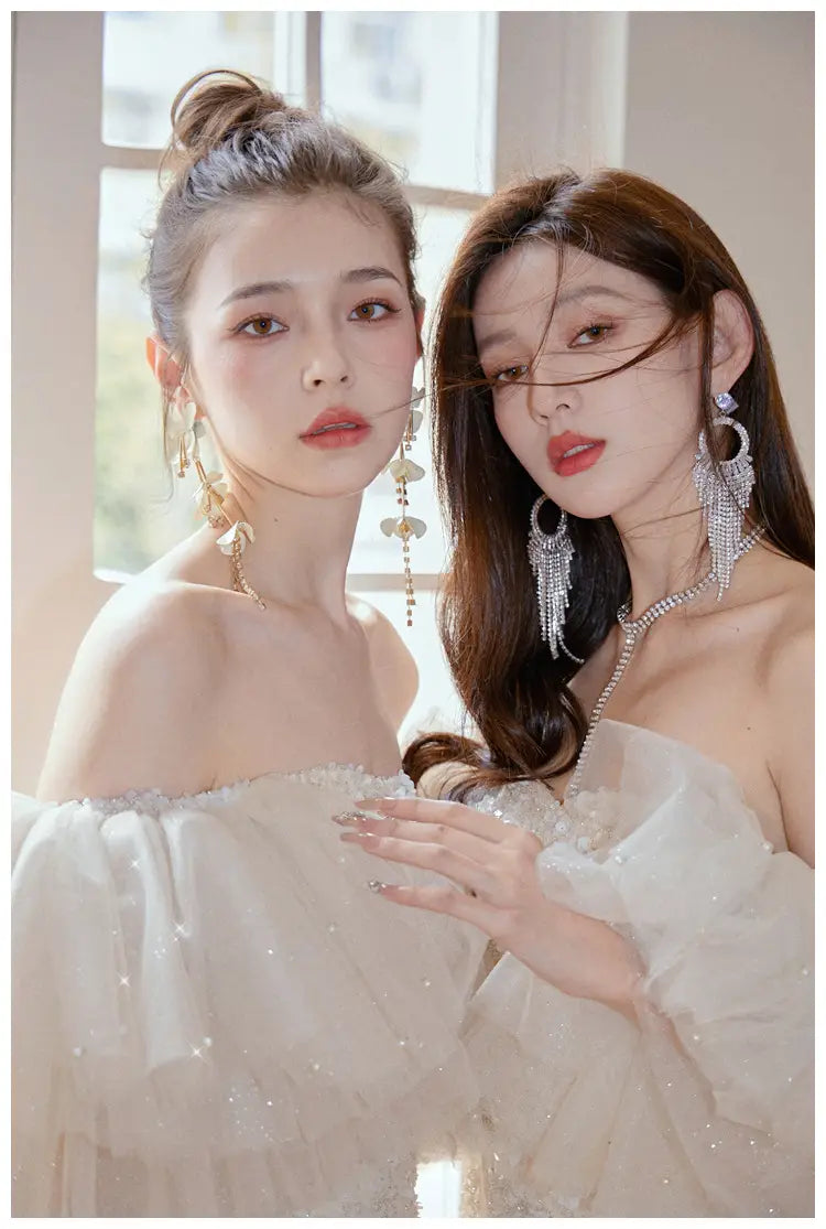 the women are wearing off-the-shoulder ivory lace cinched waist miniskirt fairy dresses with sparkling embellishments.