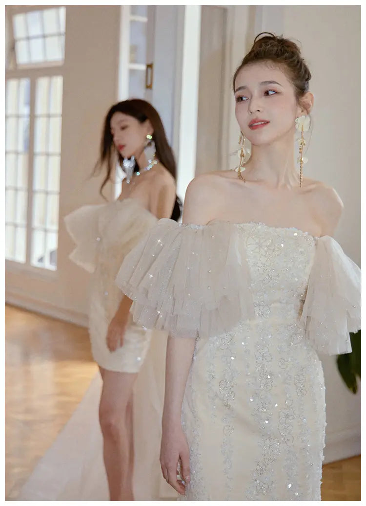an ivory lace cinched waist miniskirt fairy dress featuring a shimmering off-the-shoulder design with intricate beading and layered sheer ruffles on the sleeves.