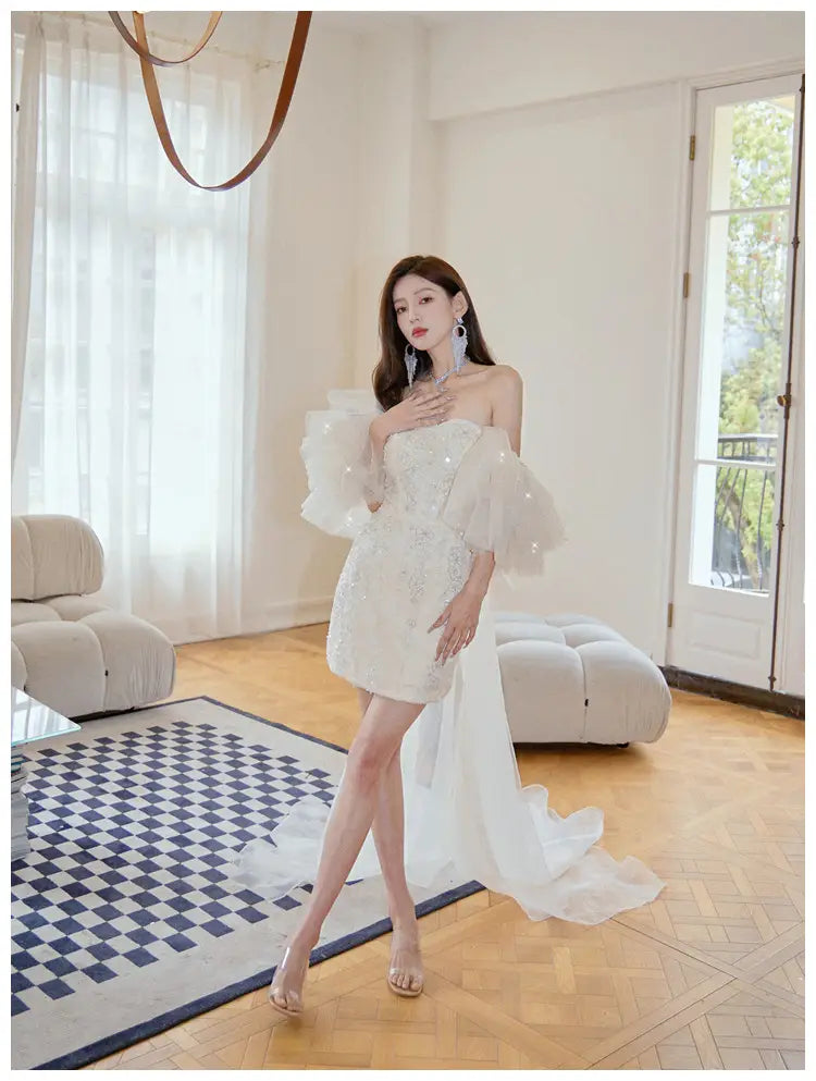 A white off-the-shoulder cinched waist miniskirt fairy dress featuring sheer puffy sleeves and a flowing train.