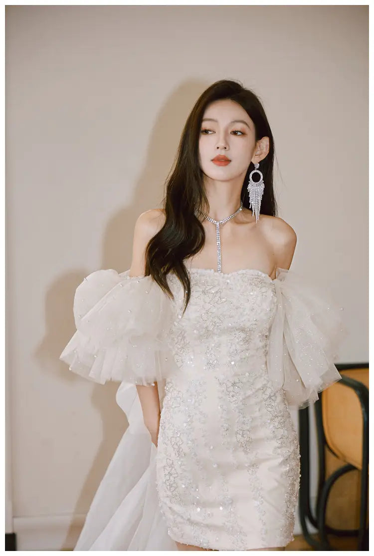 A sparkling white ivory lace cinched waist miniskirt fairy dress featuring an off-the-shoulder design with intricate beading and sheer ruffled sleeves.