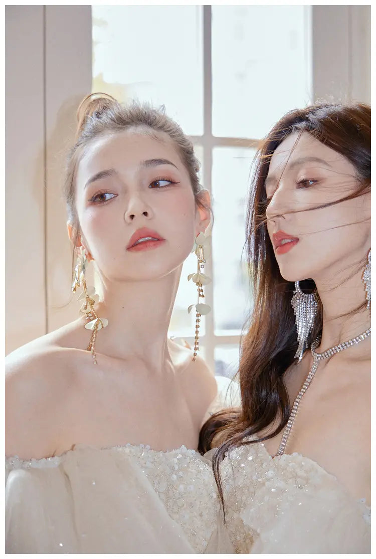 two women wearing off-the-shoulder white wedding gowns with intricate beading and lace detailing featuring a cinched waist miniskirt fairy design