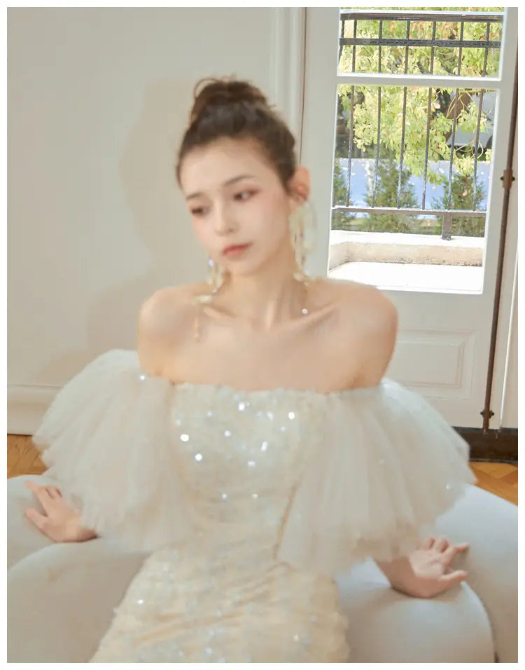 Ivory lace cinched waist miniskirt fairy dress featuring a white off-the-shoulder gown with a sequined bodice and voluminous tulle sleeves.