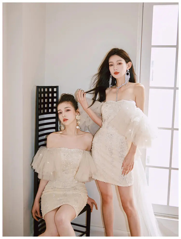 Off-the-shoulder ivory white sequined cinched waist miniskirt fairy dress with sheer ruffled sleeves and lace detailing.