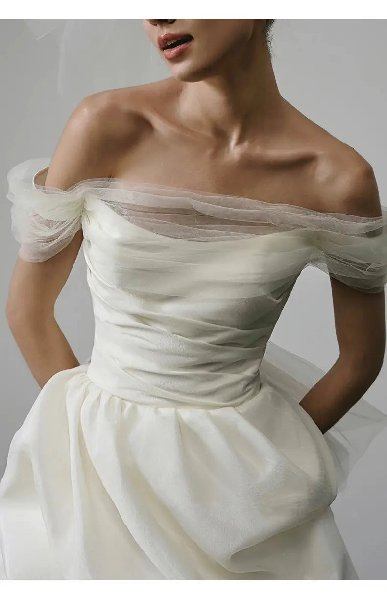 off-shoulder tulle white wedding dress featuring an ivory satin fitted bodice with sheer tulle sleeves and a flowing train in a light wedding dress design.