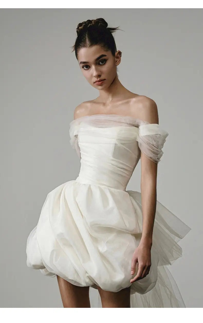 Off-shoulder white wedding dress made of light tulle with a fitted bodice and voluminous mini skirt featuring a train.