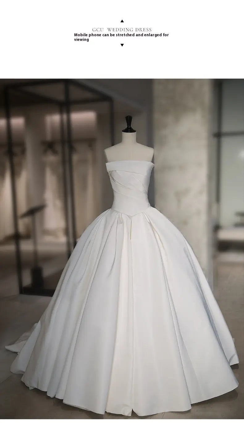 a simple elegant french style white satin wedding dress featuring an off-the-shoulder fitted bodice and a voluminous ball gown skirt