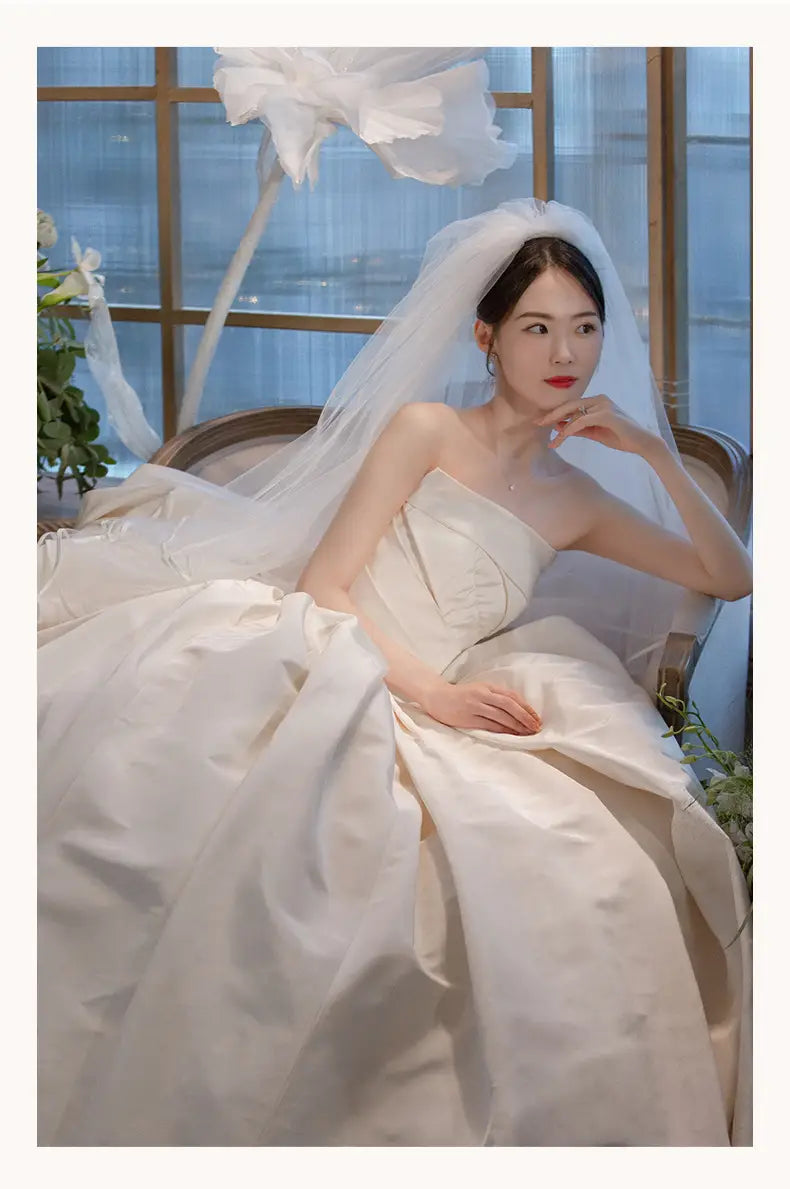 A flowing ivory satin wedding gown with a strapless bodice and a large layered skirt showcasing a simple elegant french style.