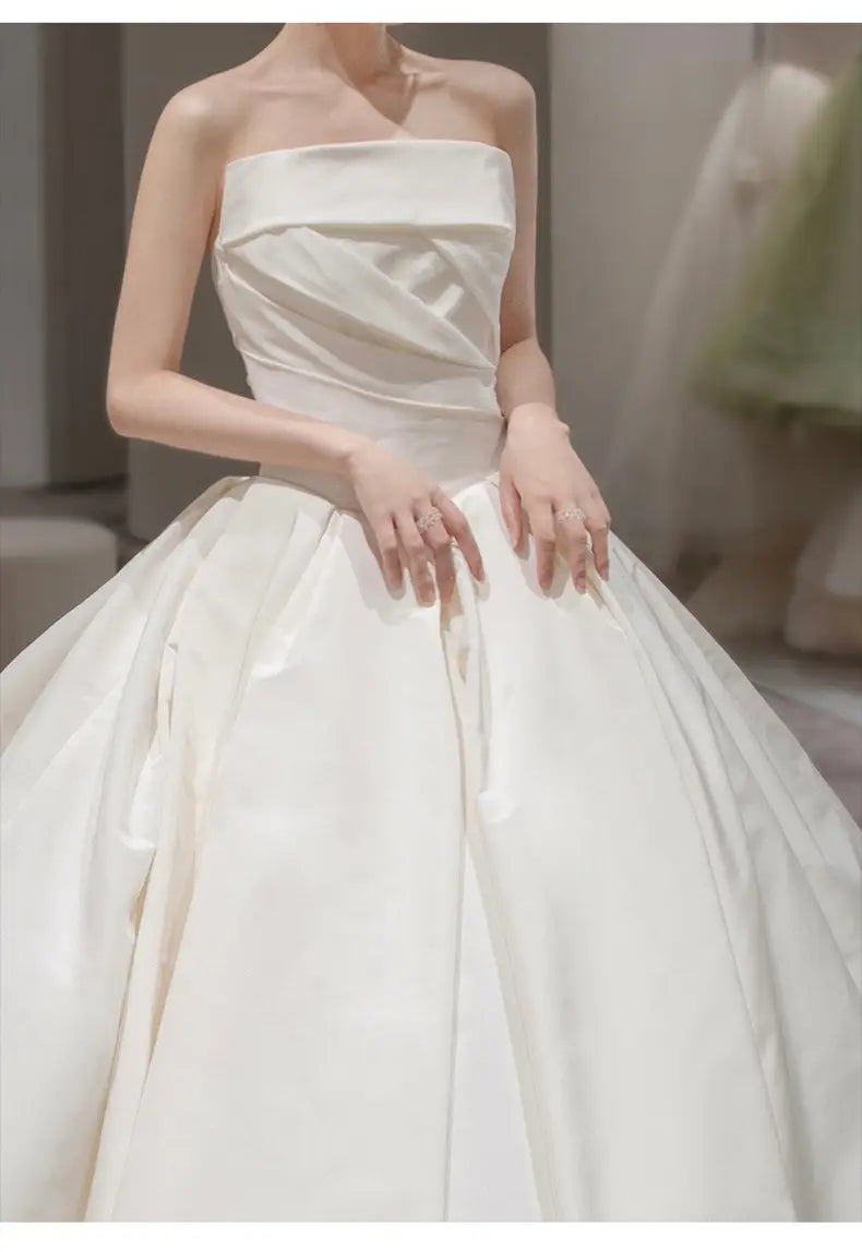 a simple elegant french style strapless ivory satin wedding gown featuring a structured bodice and a voluminous skirt