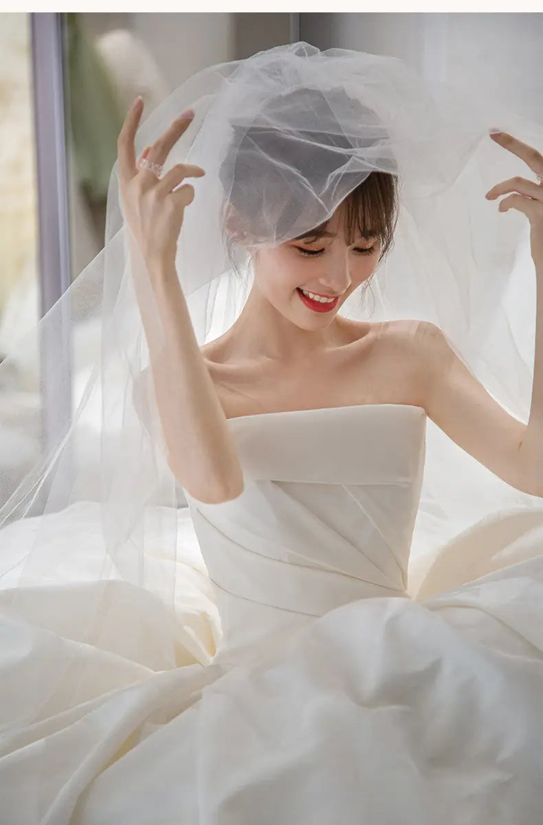 a delicate sheer white veil with a soft flowing design drapes gracefully over the bride’s head complementing the simple elegant french style satin wedding dress