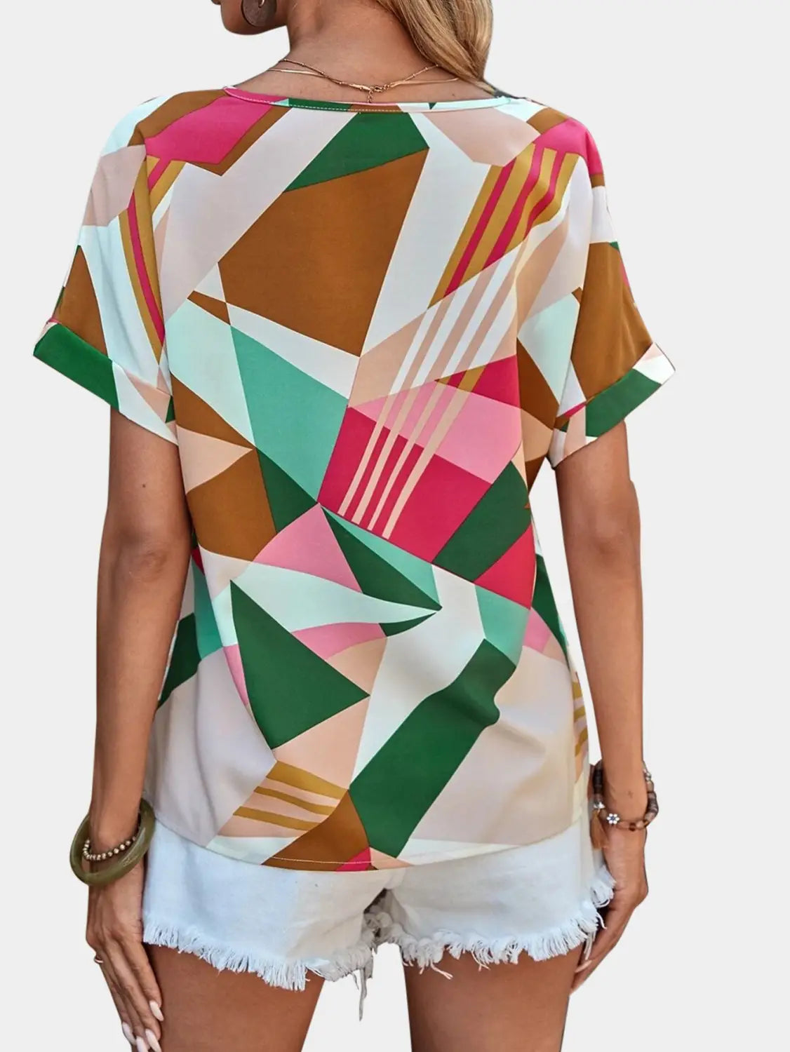 A vibrant geometric-patterned women’s clothing printed v-neck top in shades of pink, green, brown, and white with short sleeves.