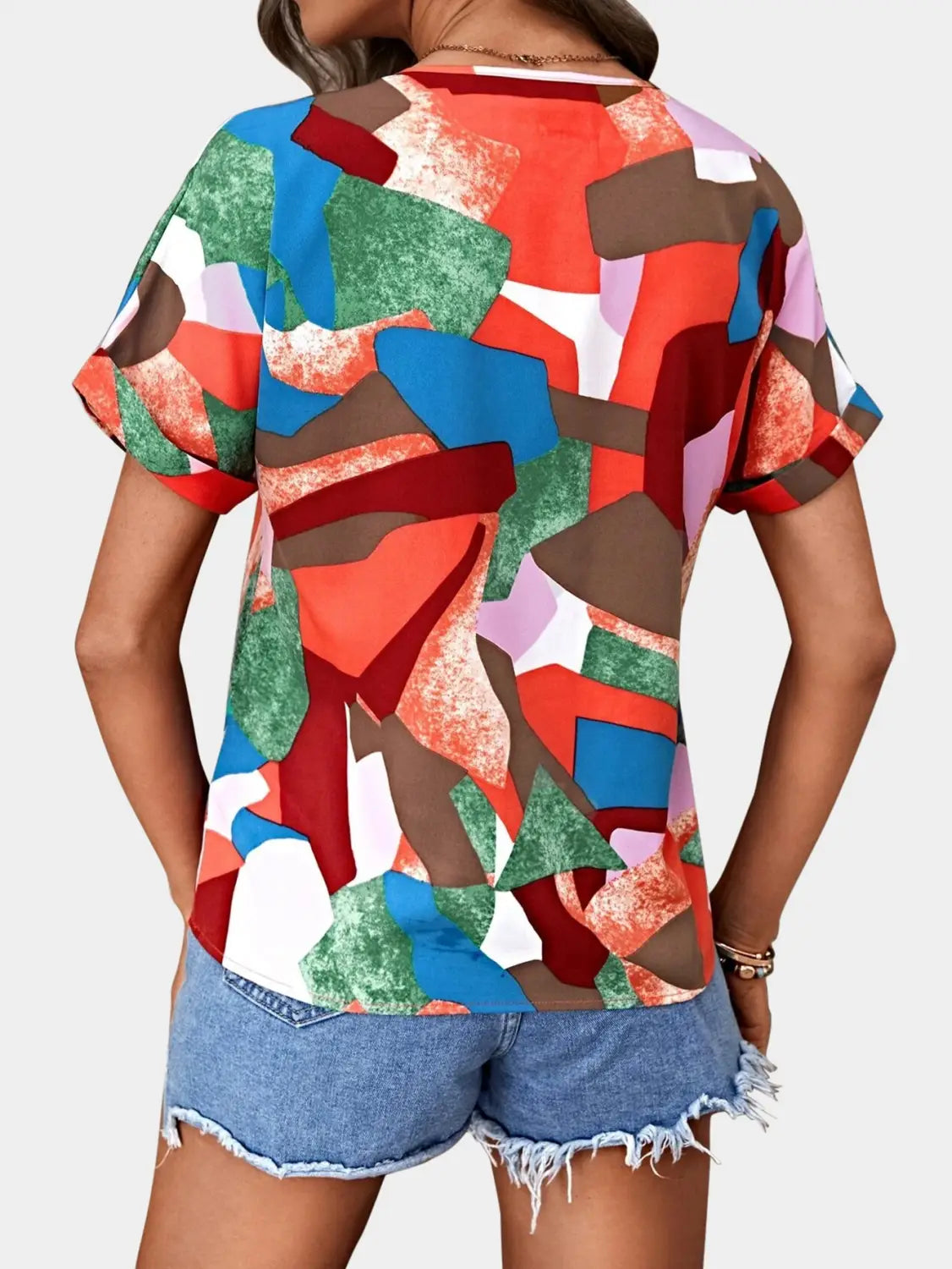 A vibrant short-sleeved women’s clothing printed v-neck top featuring a bold geometric pattern in red blue green brown and white.