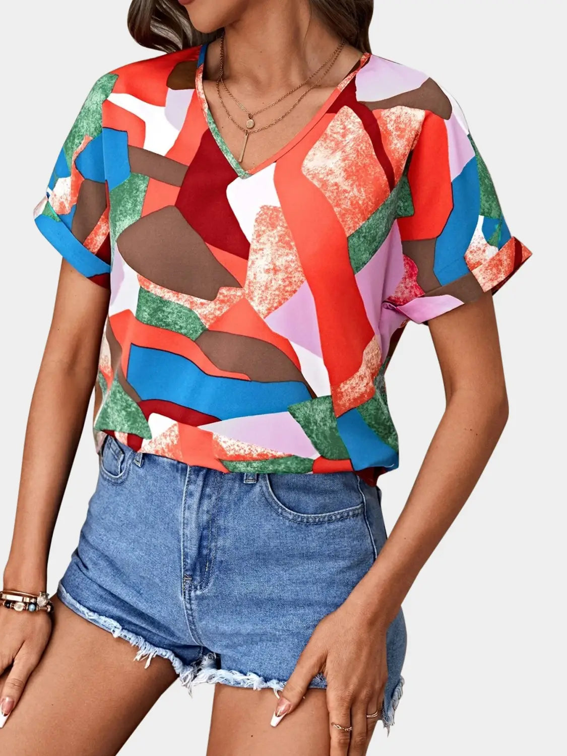A vibrant short-sleeved women’s clothing printed v-neck top featuring a bold geometric pattern in reds blues greens and purples.