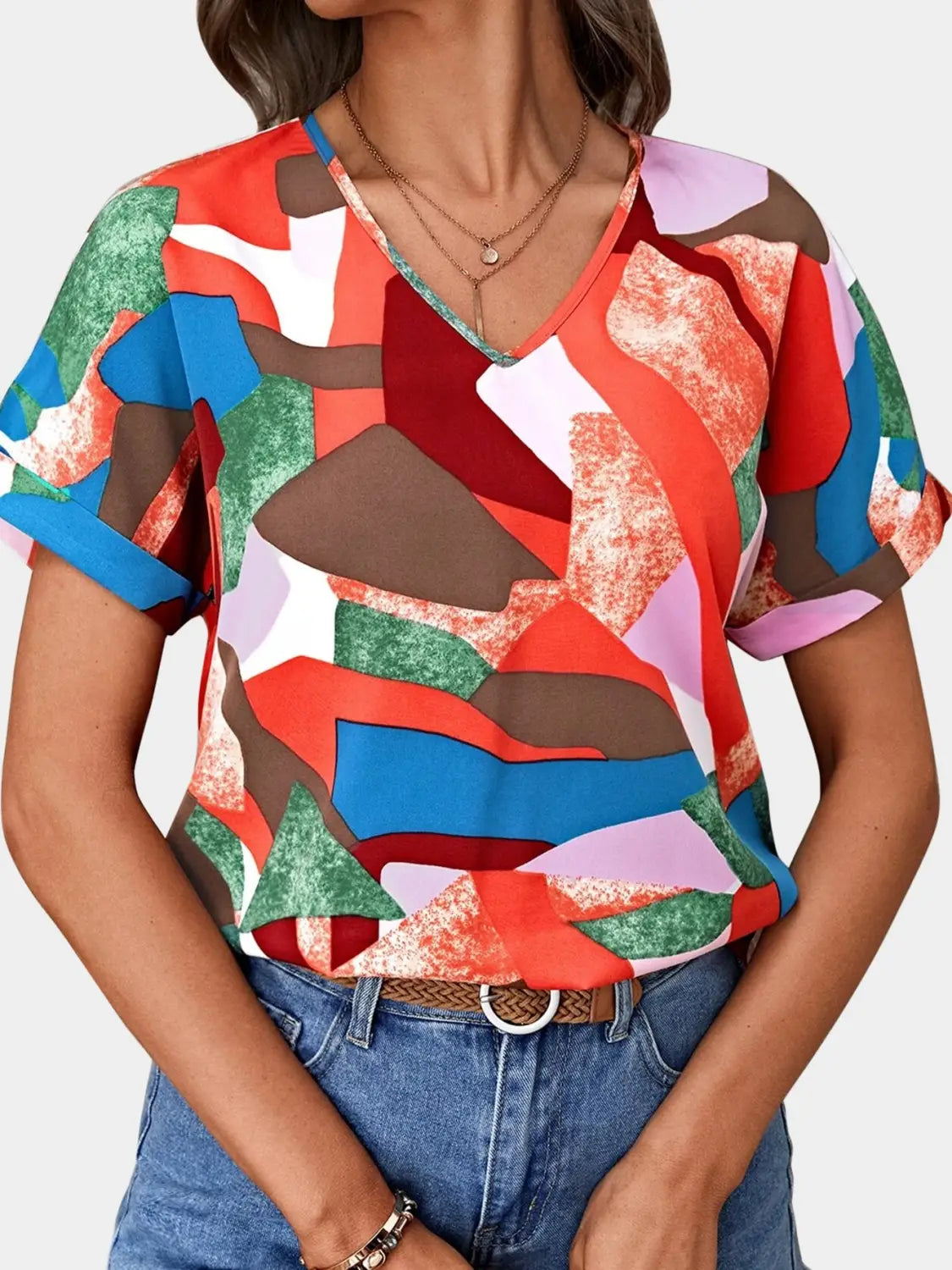 A vibrant short-sleeved geometric women’s clothing printed v-neck top with bold red blue green brown and pink abstract print on lightweight fabric.