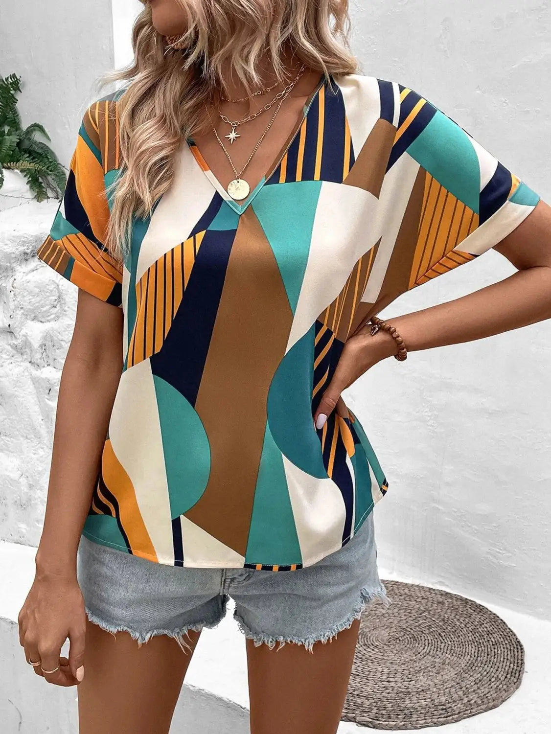 A woman wears a short-sleeved geometric women’s clothing printed v-neck top featuring bold teal orange navy blue and cream patterns.