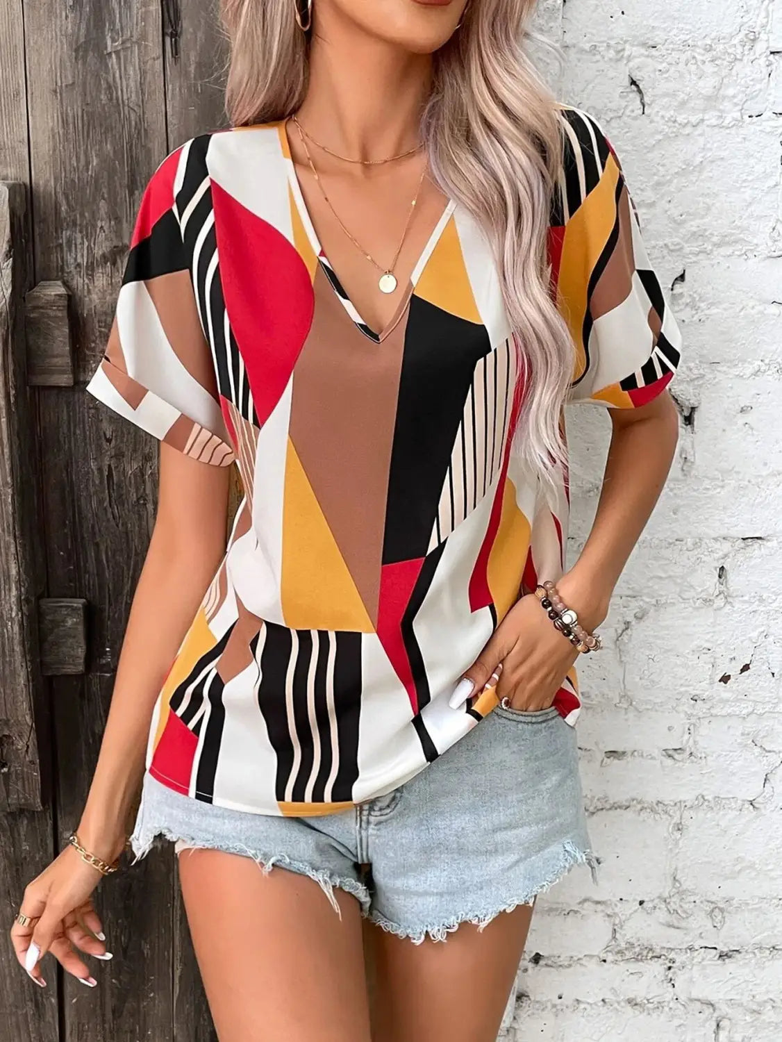 A vibrant women’s clothing printed v-neck top with short sleeves featuring a geometric pattern in red, yellow, black, and white.