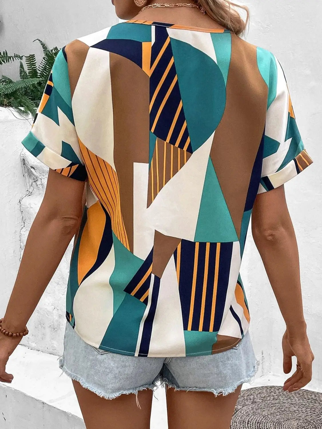 a woman wearing a short-sleeved geometric women’s clothing printed v-neck top with an abstract pattern in teal navy blue orange and white
