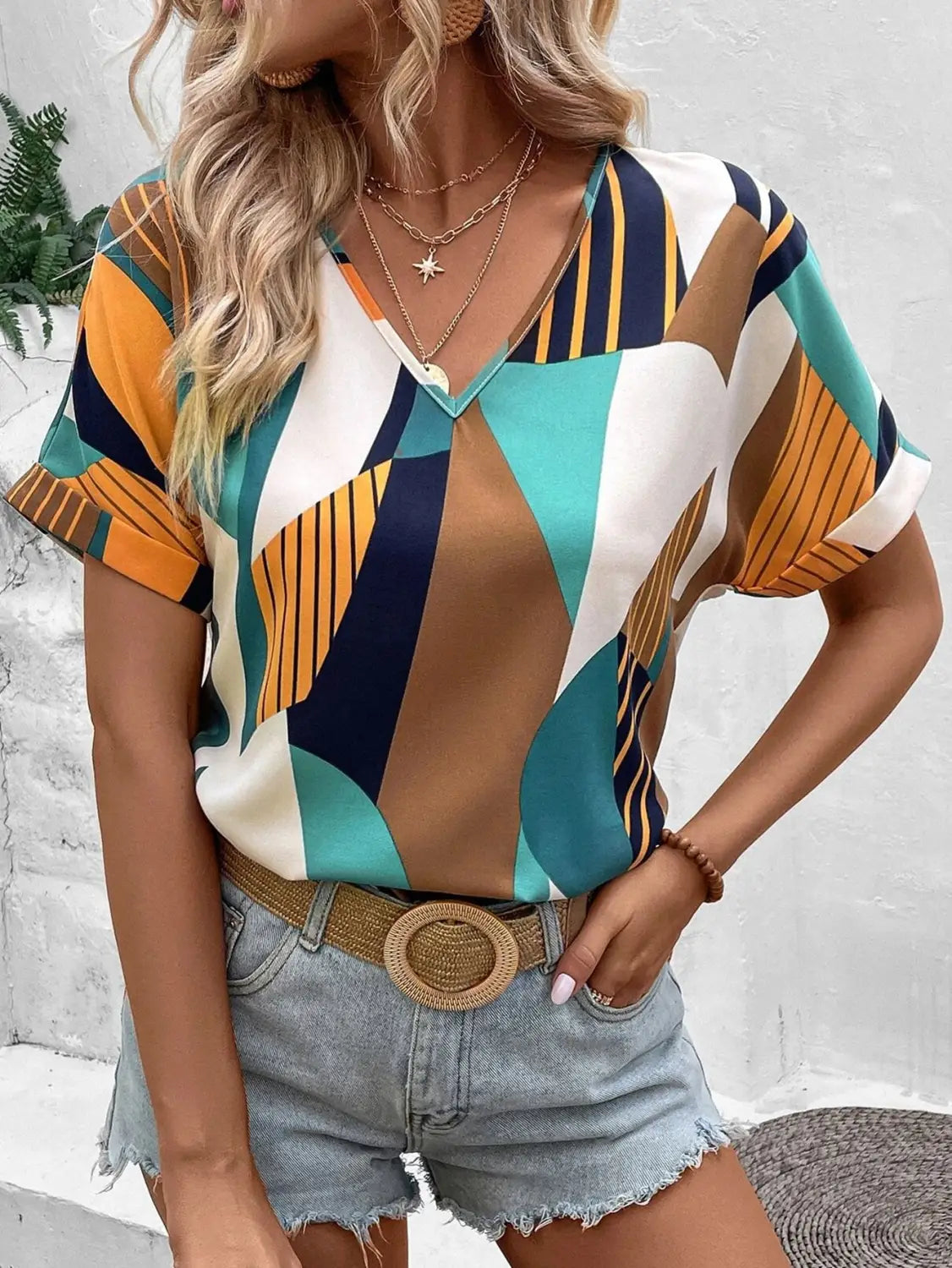 A vibrant geometric-patterned women’s clothing printed v-neck blouse in teal orange navy blue and white with short sleeves.