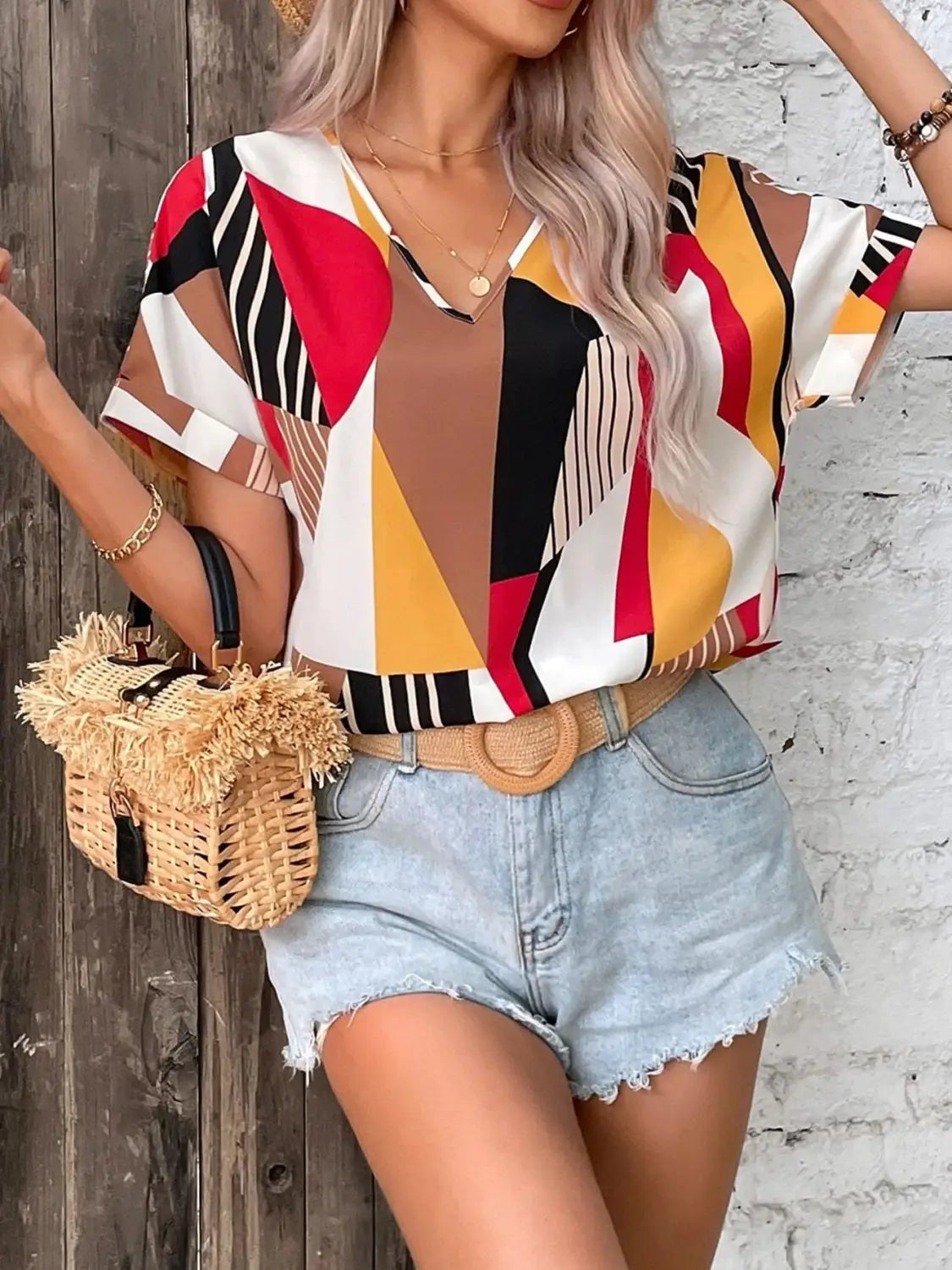 a woven straw crossbody bag with a fringed top and black leather handle paired with geometric women’s clothing printed v-neck top