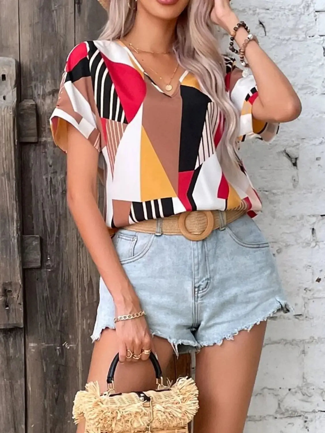 a woven straw handbag with black handles and a frayed textured top edge paired with a geometric women’s clothing printed v-neck top