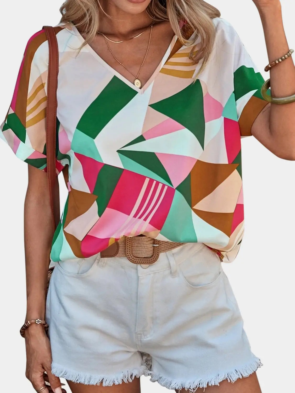A vibrant geometric-patterned women’s clothing printed v-neck top in white pink green and brown tones with short sleeves.