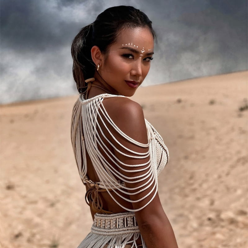 A woman wears a beige macramé tassel dress creative beach set featuring intricate woven straps and matching fringe detailing for creative beach travel.