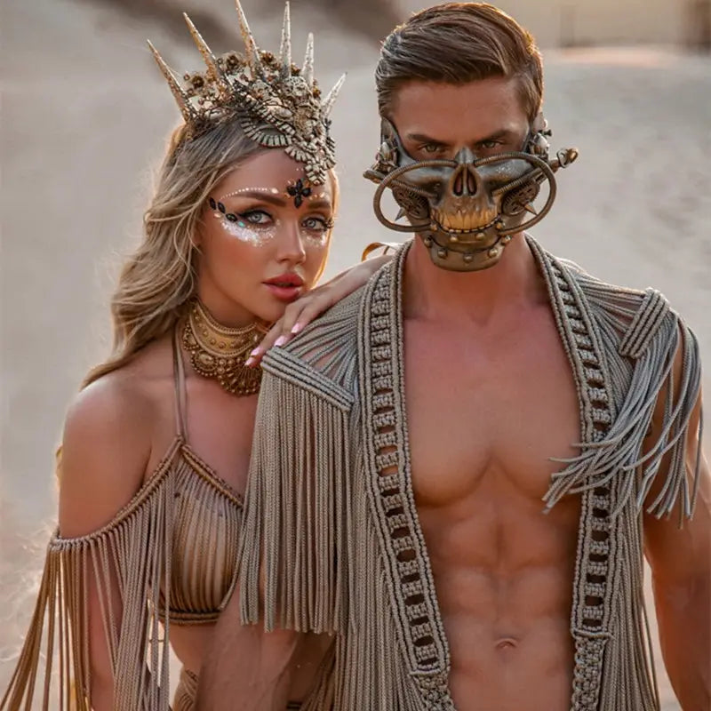 a man wearing a metallic skull-shaped mask with intricate gold detailing features alongside a beige macramé tassel dress creative beach travel set
