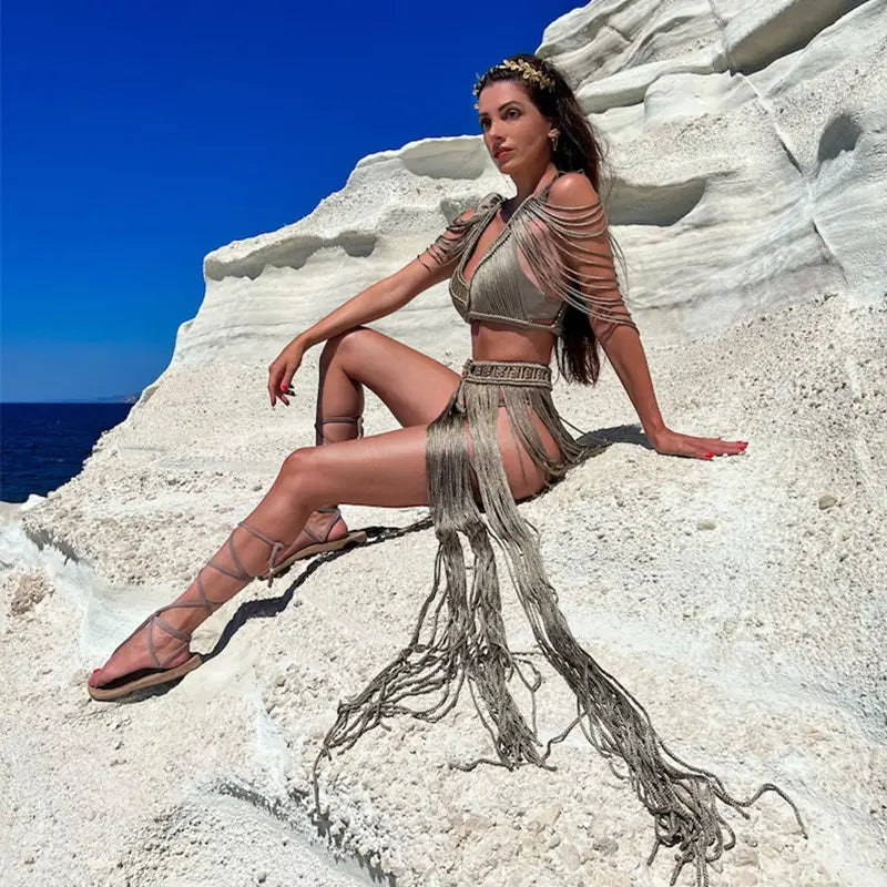 A shimmering metallic beige two-piece dress creative beach outfit with intricate fringe tassel detailing, braided design on the top piece, and a matching headpiece ideal for creative beach travel.