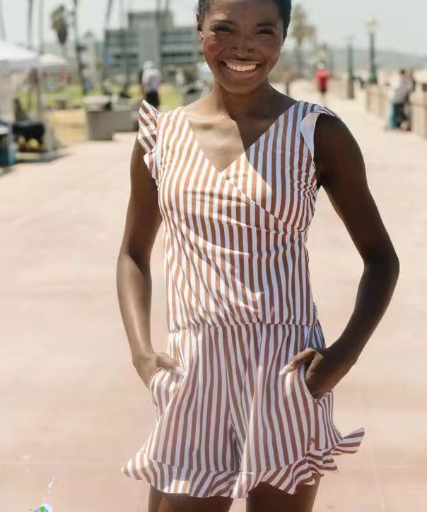 A woman wears a beige and brown vertical striped sleeveless v-neck romper with ruffled shoulder straps and hem, styled similarly to a teal ruffled deep v one-piece swimsuit with built-in bra suitable for bra hot spring or hot spring boxer use.