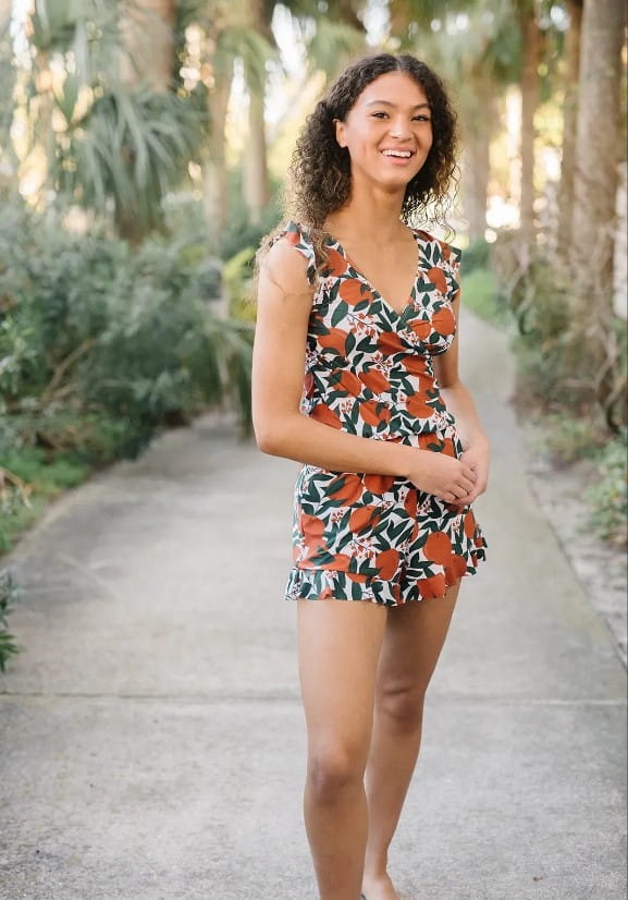 a woman wearing a sleeveless one-piece swimsuit with a teal ruffled deep v design and built-in bra featuring an orange and green leaf pattern suitable for bra hot spring use