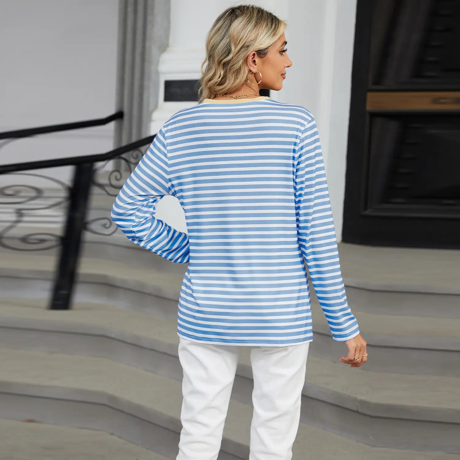 A woman wears a women’s v-neck striped loose henley top with long sleeves in light blue and white horizontal stripes.