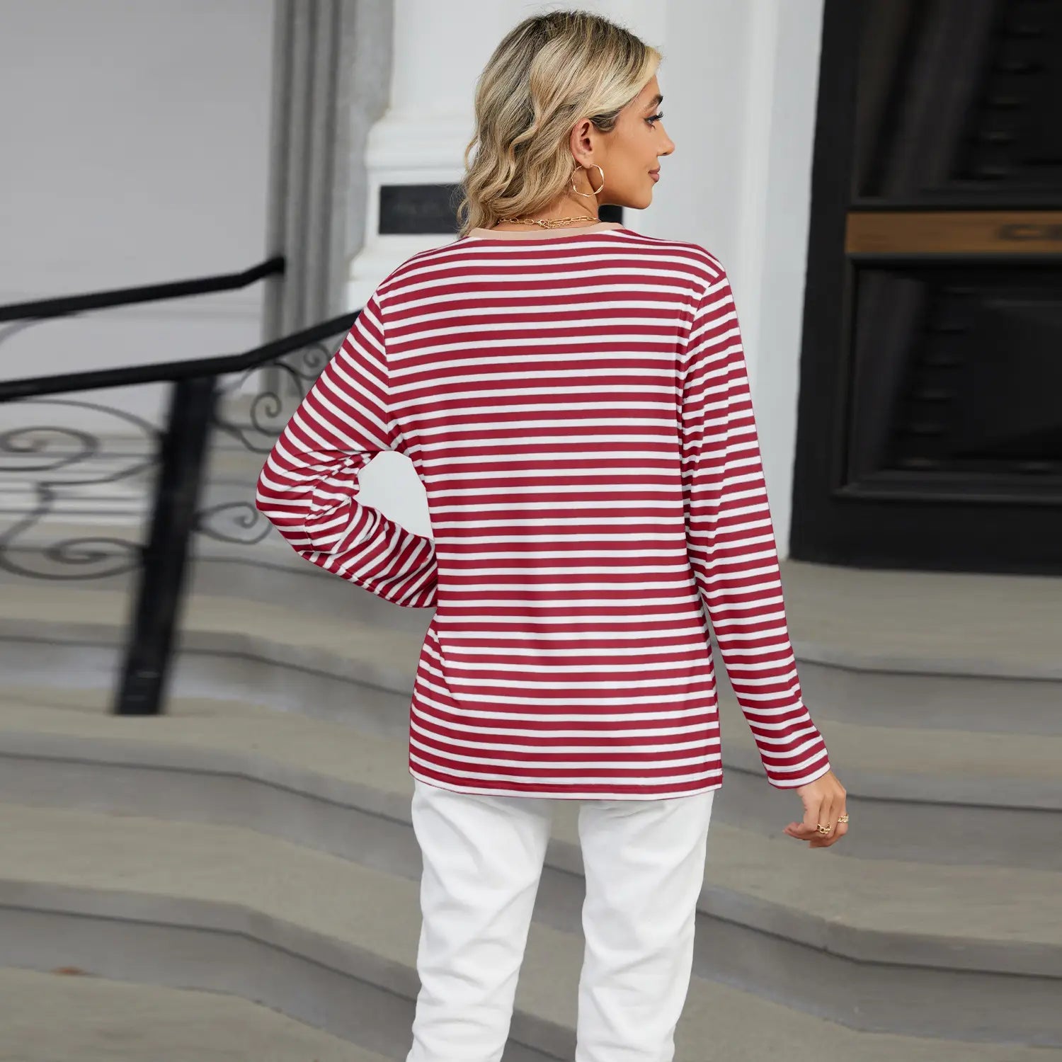 A woman wears a long-sleeved women’s v-neck striped loose henley top with red and white horizontal stripes.