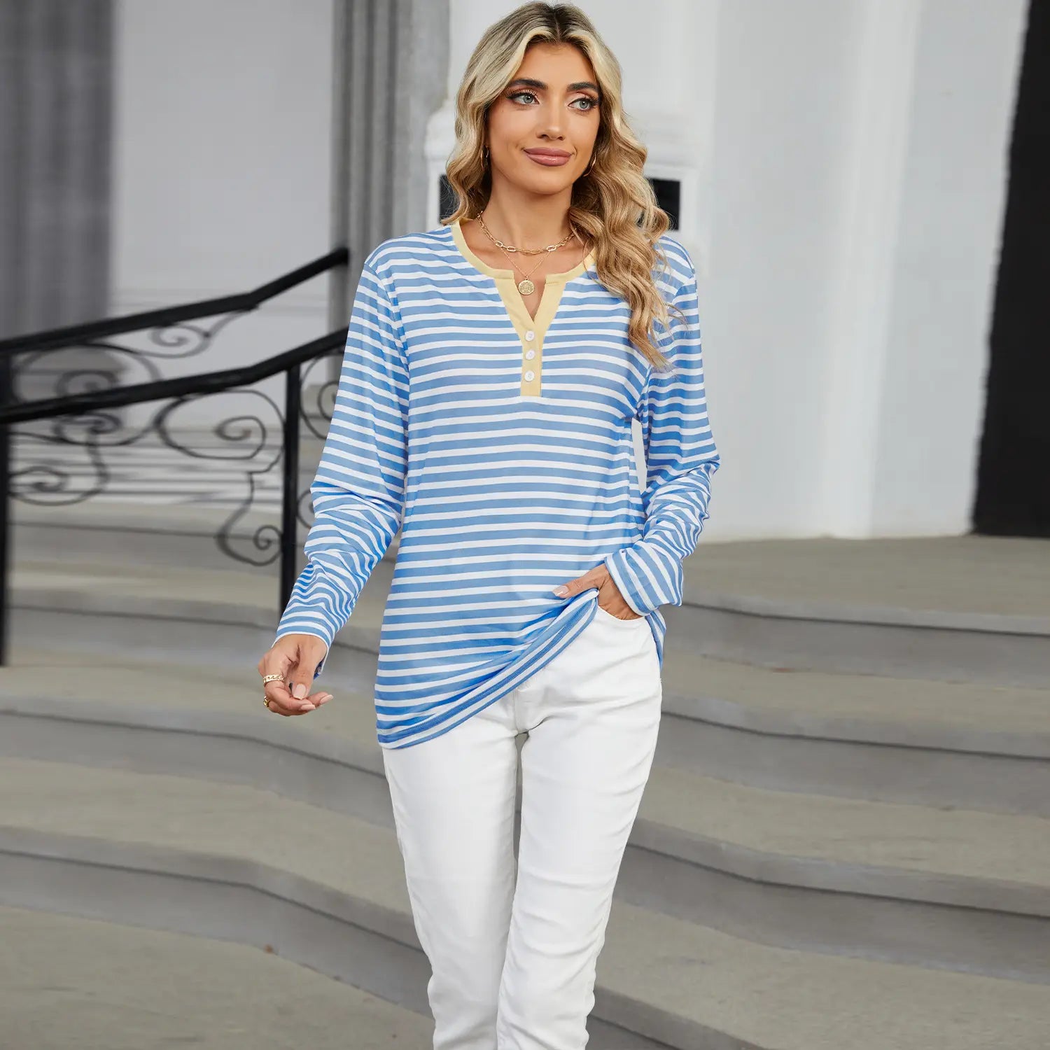 A woman wearing a women’s v-neck striped loose henley top in blue and white with a yellow button-front neckline.