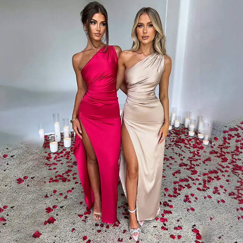 two women wearing elegant one-shoulder backless slit satin gowns, one in vibrant fuchsia and the other in a beige one-shoulder backless slit satin gown.
