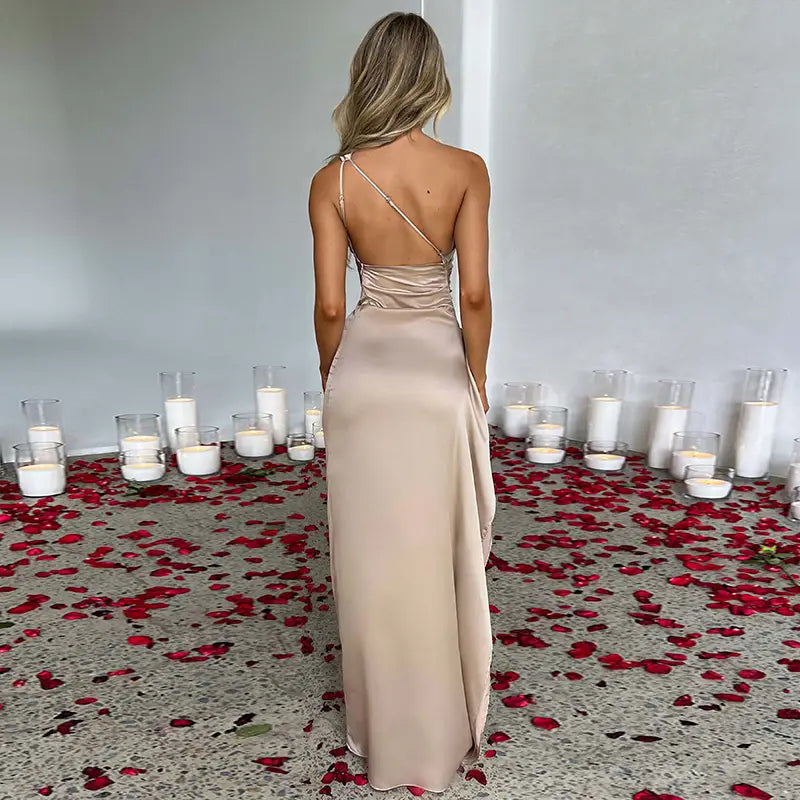 a flowing beige satin gown with a sexy one-shoulder backless design and slit showcasing elegant back detailing
